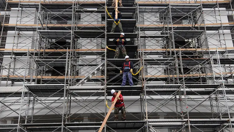 Arbeiter bauen ein Fassadengerüst an einem mehrstöckigen Gebäude ab